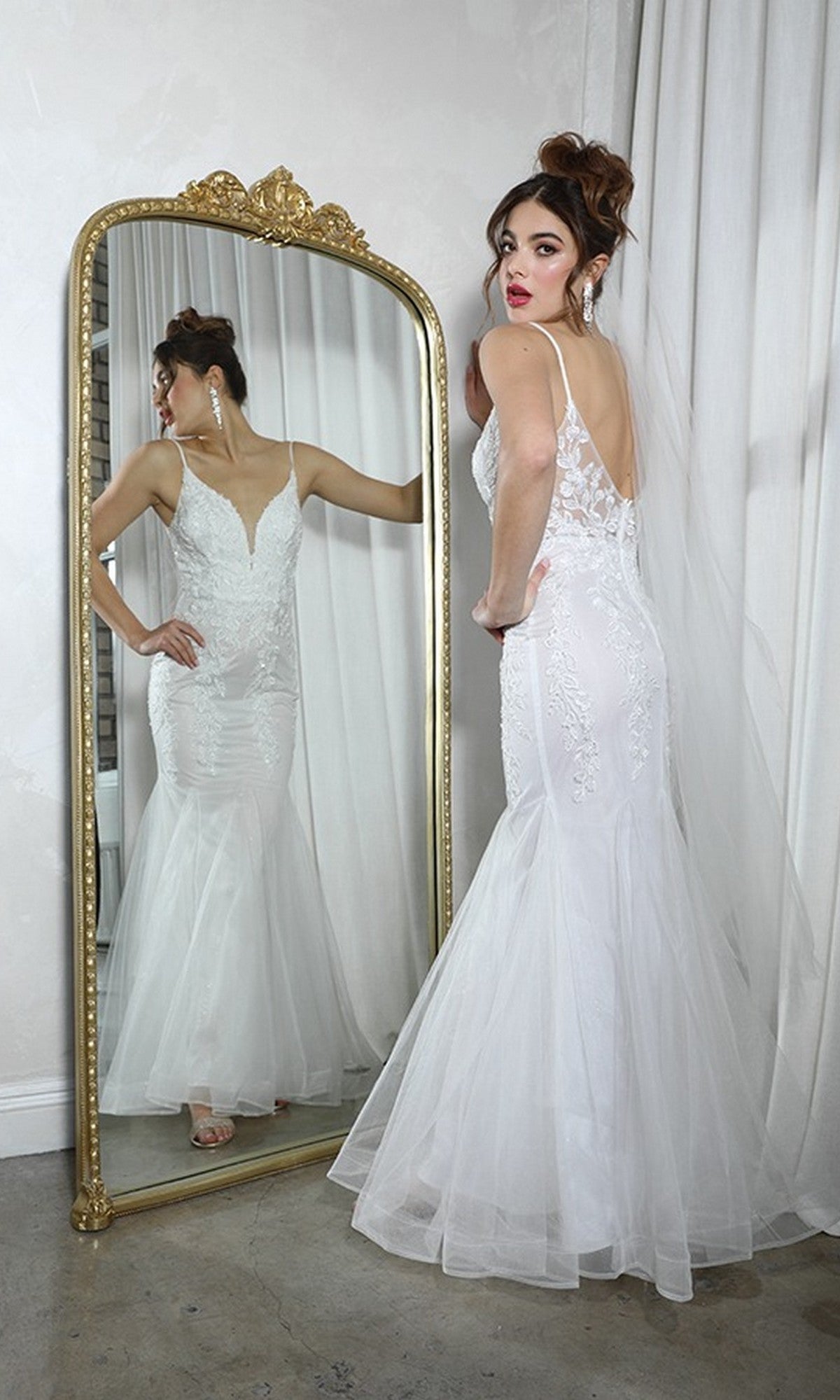 A woman in the Eureka 9998 Long Prom Dress, a fitted white lace gown with delicate beaded floral designs and veil, stands before a large ornate mirror, gazing over her shoulder at her reflection.